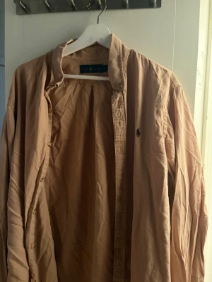 Beige manchesterskjorta Ralph Lauren XL - Säljer en beige manchesterskjorta från Ralph Lauren i storlek XL. Skjortan har klassisk krage, knappar framtill och den ikoniska lilla loggan broderad på bröstet. Perfekt för dig som gillar en avslappnad men ändå stilren look.