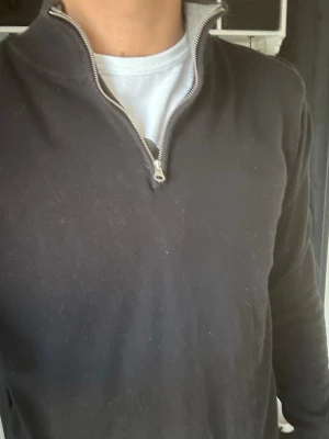 Svart halvzip tröja från John Henric - Snygg svart tröja från John Henric med halvzip och ståkrage. Tröjan har långa ärmar och ribbade muddar vid ärmslut och nederkant. Perfekt till jeans och enkel att matcha med olika stilar.