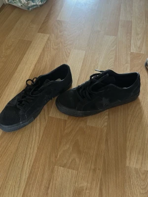 Svarta Converse One Star sneakers - Säljer ett par svarta Converse One Star sneakers i mocka med klassisk stjärndetalj på sidan. Skorna har svart sula, svarta skosnören och låg profil. Perfekta för en avslappnad streetwear-look.