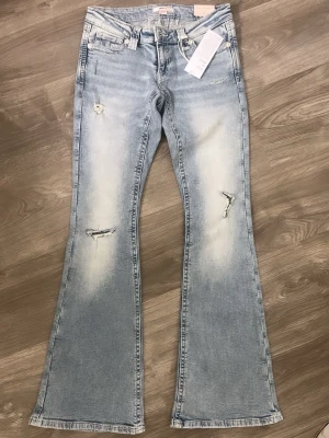 Ljusblå bootcut jeans med slitningar - Säljer ett par ljusblå bootcut jeans från Na-Kd med snygga slitningar på låren och knäna. Jeansen har klassisk femficksmodell, hög midja och utställda ben. Perfekta för dig som gillar en avslappnad men trendig stil. Dom är jeansen är helt nya men prislapp och kostade 399 men säljer för 280.