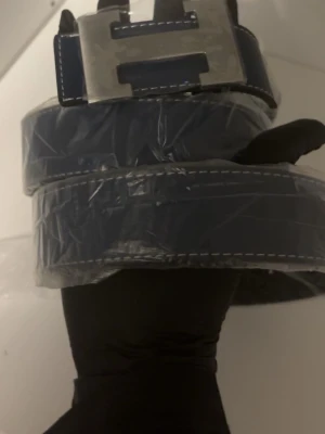 Blå/svart bälte - Snyggt blått bälte med vit kontrastsöm och ett stort, fyrkantigt metallspänne. Perfekt för att lyfta vilken outfit som helst med en cool detalj. Klassisk design som funkar till många olika stilar.