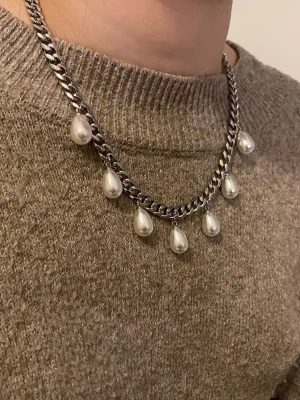 Kedjehalsband med droppformade pärlor - Snyggt halsband med en grov silverfärgad kedja och hängande droppformade vita pärlor. Kedjan har en chunky känsla och pärlorna ger en cool kontrast till metallen. Perfekt för att lyfta vilken outfit som helst med en trendig touch.