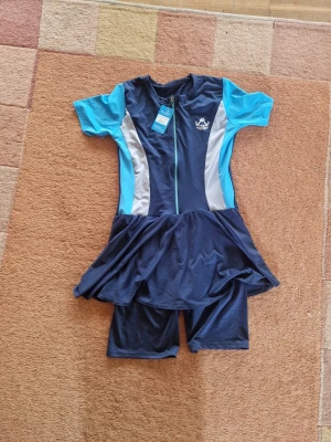 Marinblå burkini med kjol och shorts - Snygg marinblå burkini  ljusblå och grå paneler. Modellen har korta ärmar, dragkedja framtill, kjoldel och matchande shorts.