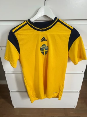 Sverige tröja - Gul och marinblå svensk landslagströja från Adidas med broderat landslagsemblem på bröstet. Endast anvönd en gång. Passar även mig som har xs/s. Perfekt nu inför vm