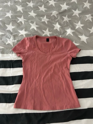 Rosa basic t-shirt med rund hals - En enkel rosa t-shirt med rund halsringning och korta ärmar. Modellen är figurnära och passar perfekt till jeans eller kjol. Tillverkad i mjukt bomullsmaterial för skön känsla hela dagen.