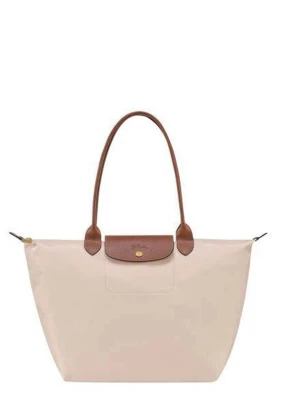 Beige Longchamp Le Pliage handväska - Stilren beige handväska från Longchamp, modell Le Pliage, med bruna läderhandtag och lock. Väskan är tillverkad i slitstark nylon med detaljer i läder och har en klassisk, rymlig tote-form. Perfekt för dig som gillar enkel och tidlös design. Väskan är något smutsig och har en fläck på framsidan som kan gå bort i tvätten. 