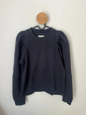 Mörkblå sweatshirt med puffärm från Second Female - Mörkblå sweatshirt från Second Female i storlek M. Tröjan har puffade axlar och långa ärmar, samt ribbade muddar vid ärmslut och halsringning. Tillverkad i bomull. Hör av dig vid frågor och funderingar! 