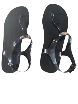 Svarta jellysandaler med spänne - Snygga svarta sandaler i jellymaterial med tårem och justerbart spänne vid ankeln. Sandalerna har en minimalistisk design och silverfärgade detaljer vid remmarna. Perfekta för sommardagar och strandhäng.