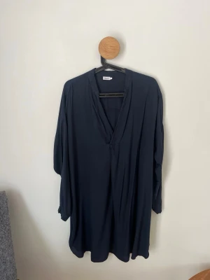Mörkblå klänning från Filippa K - Stilren mörkblå klänning från Filippa K med v-ringad hals och lång ärm. Klänningen har en lös passform och är tillverkad i ett mjukt, lätt material. Hör av dig vid frågor och funderingar! 