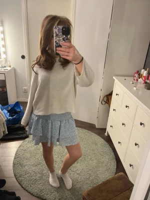 Blå blommig volangkjol - Söt kort blå kjol med små vita blommor och volangdetaljer. Kjolen har en luftig och flowy passform, perfekt för varmare dagar. Resår i midjan för extra komfort och enkel styling.