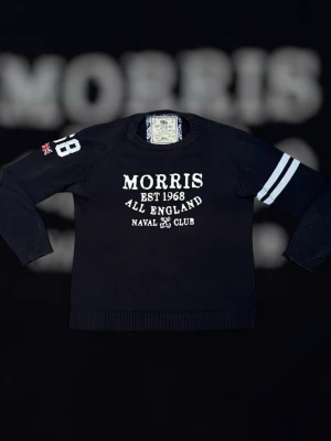 Marinblå tröja från Morris - Snygg marinblå tröja från Morris med vit text och tryck på bröstet, samt siffran 18 och brittisk flagga på ena ärmen. Två vita ränder på andra ärmen ger en sportig look. Rund halsringning och ribbade muddar.