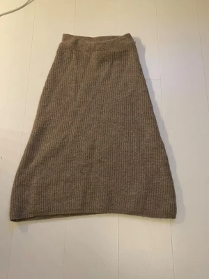 Beige stickad långkjol - Mysig beige stickad långkjol med ribbad struktur. Kjolen har en enkel och klassisk design som är lätt att matcha med olika toppar. Perfekt för dig som gillar en avslappnad och trendig stil under kyligare dagar.