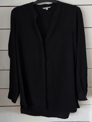 Svart blus från Happy Holly - Stilren svart blus från Happy Holly med v-ringad hals och långa ärmar. Blusen har en avslappnad passform och är tillverkad i ett mjukt, lätt material som ger en skön känsla. Perfekt att matcha med jeans eller kjol för en trendig look.