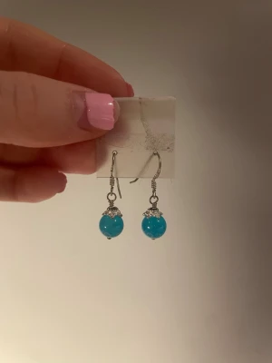 3 nya par örhängen  - Säljer 3 par örhängen med  pärlor. Ett par har klara turkosa runda pärlor med silverfärgade detaljer, det andra paret har ljusblå facetterade pärlor. Båda paren har krokar i metall och enkel, stilren design.