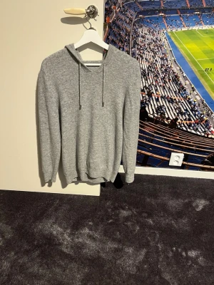 Grå chasmire hoodie -  Jag säljer denna stilrena gråa hoodie i chasmire eftersom den har blivit för liten. Tröjan har långa ärmar och ribbade muddar vid ärmslut. Passar dig som gillar enkel och klassisk stil. Den är i bra skick och den enda defekten den har är att kragen har lossnat lite