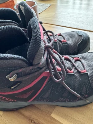 Salomon Gore-Tex kängor grå/rosa - Säljer ett par Salomon kängor med Gore-Tex, perfekta för utomhusaktiviteter. De är grå med rosa detaljer, har snörning och är tillverkade i slitstarkt syntetmaterial och mesh. Skorna har hög komfort och bra grepp för vandring och äventyr.