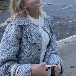 Blåvit teddyjacka med krage - Säljer en blommig jacka med krage och knappar framtill. Jackan har en mjuk, fluffig textur och en avslappnad passform som ger en trendig look. Perfekt för dig som vill ha en mysig och snygg jacka till vardags.
