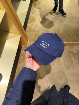 Mörkblå keps Not From Paris Madame - Snygg mörkblå keps från Not From Paris Madame med broderad vit text framtill. Klassisk böjd skärm och justerbar rem bak. Perfekt accessoar för en clean och trendig look. Tillverkad i bomull för skön känsla.