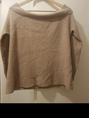 Beige stickad tröja med bred krage - Säljer en beige stickad tröja med, off shoulder, bred, nedvikt krage och långa ärmar. Tröjan har en rak passform och är ribbstickad vilket ger en snygg struktur. Perfekt för dig som gillar en enkel men stilren look. Storlek: s/m