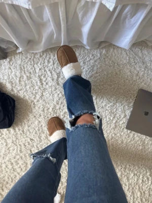 Blå slitna bootcut jeans - Säljer ett par blå bootcut jeans med slitningar och hål vid knäna. Jeansen har dubbla knappar framtill och klassiska fickor. Perfekta för en avslappnad och trendig look.