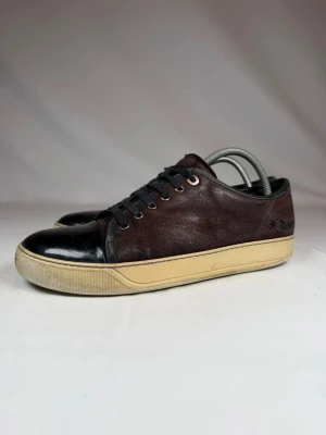 Mörkbruna sneakers med svart tå - Sneakers i mörkbrunt mocka med svart tåparti i läder, svarta skosnören och beige sula. Klassisk låg modell med metallöljetter och stilren design. Perfekta för dig som gillar en clean look med lite retrovibe. De är bara lägga ett prisförslag om du är sugen