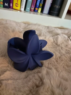 Blå hårklämma i blomform - Snygg hårklämma i matt mörkblå plast med blomformad design. Perfekt för att snabbt sätta upp håret med en cool och trendig look. Klämman har stora blad och känns stabil i handen.