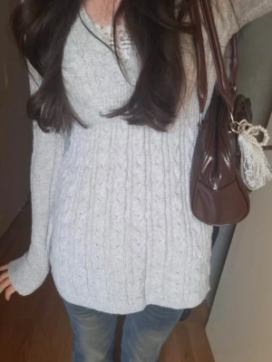 Ljusgrå kabelstickad tröja - Mjuk figurnära stickad topp med V-ringning och smickrande midja. Väldigt trendig modell som ger babydoll/Y2K vibe – perfekt till stövlar, tights eller jeans.  🤍 Mysig höst/vår favorit 📦 Samfrakt finns – kolla gärna mina andra annonser! Mycket bra skick Strl: s   