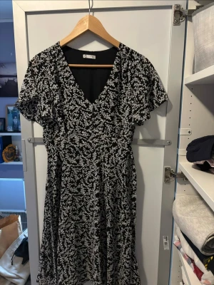 Svartvit blommig klänning - Säljer nu denna svarta klänningen med vitt blommigt mönster då den inte längre kommer till användning. Klänningen har knytband runt midjan och en dragkedja på sidan.
