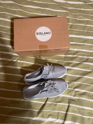 Grå sneakers från Bielano - Snygga grå sneakers från Bielano med vit sula och meshmaterial på ovansidan. Skorna har klassiska snörningar och en modern, sportig design. Perfekta för dig som gillar stilrena och bekväma skor. Kommer med originalkartong. Skorna är aldrig använda då jag köpte de och de kom aldrig till användning, storleken är 41 men skorna är rätt flexibla så de passar både mindre & Större storlekar. Priset är 200 men kan gå ner vid snabbaffär. Om du vill ha fler bilder eller så är det bara att hojta till!