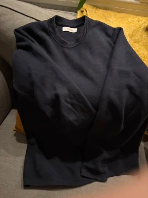 Mörkblå rundhalsad tröja  - En stilren mörkblå tröja  med rund halsringning och långa ärmar. Tröjan har en enkel, klassisk design och är tillverkad i ett mjukt material som passar perfekt till olika outfits.