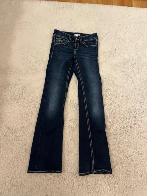 Mörkblå bootcut jeans - Snygga mörkblå bootcut jeans med vita kontrastsömmar och detaljerad ficka fram. Jeansen har låg midja och klassisk femficksdesign. Perfekta för en avslappnad och trendig look. 