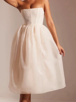 Ljus axelbandslös kortklänning - Superfin axelbandslös klänning i ljus ton med puffig kjol och strukturerad överdel. Kjolen är voluminös och ger en romantisk vibe, perfekt för speciella tillfällen. Materialet ser ut att vara en mix av polyester och eventuellt siden för extra lyxig känsla.