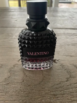 Valentino Uomo Born In Roma Intense - Valentino Uomo Born In Roma Intense EdP är en lyxig parfym i en cool, svart och transparent glasflaska med nitar och rosa detaljer. Flaskan har en unik, edgy design och rymmer 50ml. Den är sparsamt använd och kanske 42ml kvar. Doften är intensiv och modern, perfekt för dig som vill sticka ut.