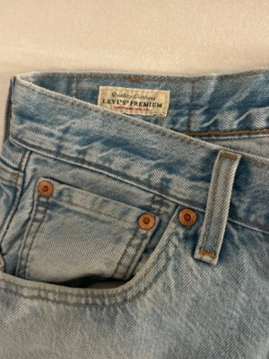 Levi's 501 ljusblå jeans - Klassiska Levi's 501 jeans i ljusblå denim med raka ben och femficksmodell. Jeansen har den ikoniska läderpatchen bak och röd Levi's-tagg på bakfickan. Snygga kontrastsömmar och kopparfärgade nitar ger en tidlös look. Perfekta för en avslappnad stil.