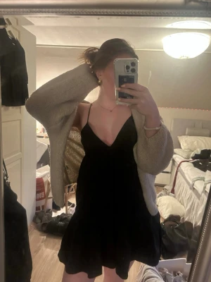 Svart kort klänning med tunna axelband - Svart kort klänning med v-ringning och tunna axelband. Klänningen har en luftig passform och volang nertill, perfekt för varma dagar. Enkel och stilren design som är lätt att matcha med olika accessoarer.