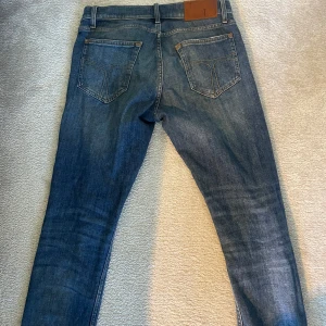 Blå jeans från Tiger of Sweden - Snygga blå jeans från Tiger of Sweden i modellen Pistolero. De har en klassisk femficksdesign med dragkedja och knapp framtill. Perfekta för en stilren look.