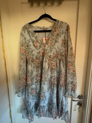 Blommig kortklänning från ONLY - Supersöt kortklänning från ONLY i ljusblått med blommigt mönster i rosa och grönt. Klänningen har v-ringning, volangdetaljer och långa ärmar. Perfekt för sommarens alla tillfällen! Den har inte kommit till användning då ni ser att prislappen sitter kvar, köpte den förra sommaren men jag tyckte inte jag passade i den.