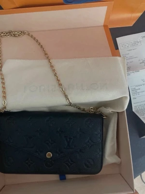 Svart Louis Vuitton handväska i läder - Säljer en svart handväska från Louis Vuitton i präglat läder med klassiskt monogrammönster. Väskan har guldfärgad kedjerem och tryckknapp. Medföljer matchande korthållare och plånbok i samma material och mönster. Perfekt för dig som gillar lyxiga accessoarer. Kvitto och box finns 🩷