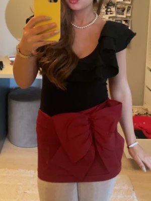 Vinröd kortkjol med stor rosett - Supersnygg vinröd kortkjol med en stor dekorativ rosett framtill. Kjolen har en tight passform och är perfekt för dig som vill sticka ut. Materialet känns som polyester och kjolen har en modern look som passar till många olika stilar.