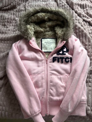 Rosa teddyjacka från Abercrombie & Fitch - Söt rosa teddyjacka från Abercrombie & Fitch med mjukt fuskpälsfoder i luvan. Jackan har dragkedja framtill, ribbade muddar och broderad logga på bröstet. Perfekt för dig som vill ha en mysig och trendig look.🤍💕Säljs eftersom den inte passar mig längre. Pris kan diskuteras 