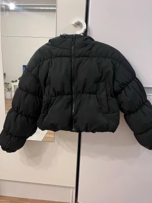Svart pufferjacka från H&M - Säljer en svart pufferjacka från H&M Divided i storlek XXS. Jackan har en croppad passform, dragkedja framtill och två fickor. Tillverkad i ett glansigt syntetmaterial som håller värmen under kalla dagar. Perfekt för dig som vill ha en trendig och varm vinterjacka. Nypris 399kr och slutsåld!