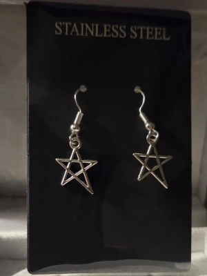 Stjärnformade örhängen i stål - Säljer ett par silvriga örhängen i rostfritt stål med öppen stjärnformad design. De har krokar för enkel användning och en stilren, minimalistisk look som passar till många olika stilar. Perfekta för dig som gillar unika accessoarer. Ca 1,5 cm. 