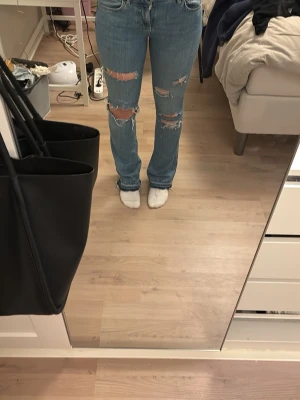 Ljusblå ripped straight jeans - Egen gjorda hål. Säljer ett par ljusblå jeans med raka ben och flera slitningar och hål på framsidan. Jeansen har klassisk femficksmodell och hög midja. Perfekta för en avslappnad och trendig look. Materialet är denim i bomull.