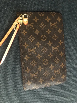 Louis Vuitton monogram plånbok - Snygg brun plånbok från Louis Vuitton med klassiskt monogrammönster och beige innerfoder med ränder. Plånboken har dragkedja och avtagbar handledsrem i ljust läder. Perfekt för kort, cash och smågrejer.