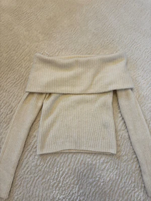 Off shoulder stickad tröja H&M - Krämvit ribbstickad off shoulder-tröja från H&M. Tröjan har långa ärmar och bred nedvikt kant över axlarna för en trendig look. Mjuk och skön kvalitet, perfekt för att lyfta din outfit med en stilren touch.
