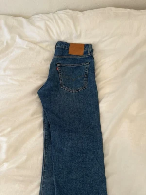 Blå Levi's raka jeans 502 - Klassiska blå jeans från Levi's med rak passform och femficksdesign. Jeansen har den ikoniska läderpatchen bak i midjan och röd Levi's-tag på bakfickan. Tillverkade i slitstark denim, perfekta för en avslappnad och tidlös stil.