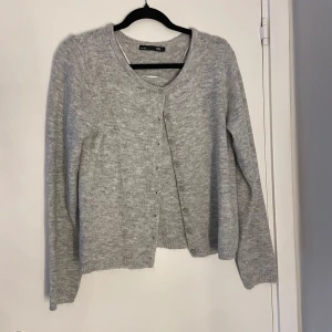 Ljusgrå kofta från 157 - Mysig ljusgrå kofta från 157 med rund halsringning och knappar framtill. Koftan har en enkel och avslappnad passform med ribbade muddar vid ärmslut och nederkant. Perfekt att slänga över en t-shirt för en chill look.