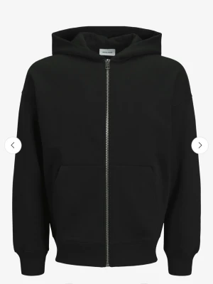 Svart hoodie med dragkedja Jack & Jones - Klassisk svart hoodie från Jack & Jones med dragkedja framtill och två stora fickor. Hoodien har en rymlig huva. Använd 1 gång