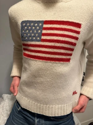 Ralph Lauren 100% Lammull I L - Ralph Lauren vit lammulströja med USA motiv. Tröjan är genuint en av de finast stickade tröjorna jag har sett, materialet är av högsta kvalitet. Tröjan är av tjock lammull. Storleken är L men i och med att det är en Unisex tröja är storleken närmare L för tjejer och M/S för killar. Hör av dig vid frågor eller prisförslag!