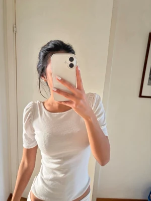 Vit ribbad topp med puffärm - Säljer en vit ribbad topp med puffärmar och rund halsringning. Toppen har en slim passform och är tillverkad i ett mjukt, stretchigt material som sitter snyggt på kroppen. Perfekt att styla med jeans eller kjol för en clean look.